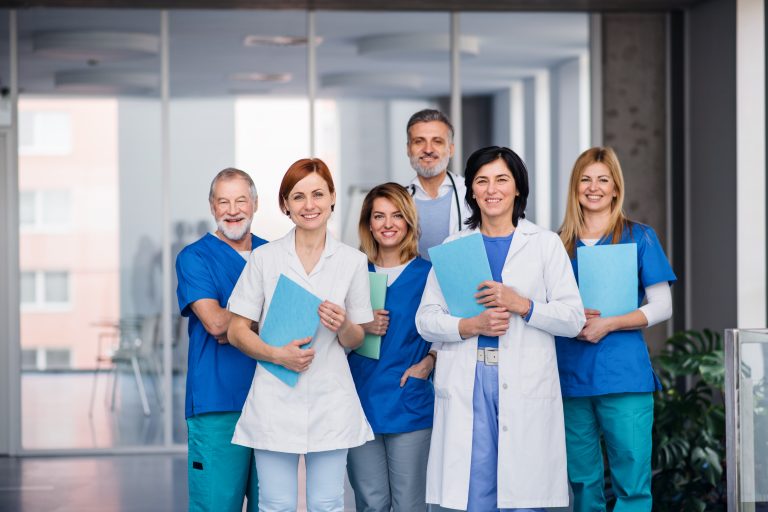 A group of six medical professionals in scrubs and lab coats stand together indoors, holding folders and smiling at the camera—reflecting healthcare innovation and the spirit of leading clinics.
